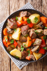pork stew with mushrooms, potatoes, carrots and peppers close-up on a plate. Vertical top view