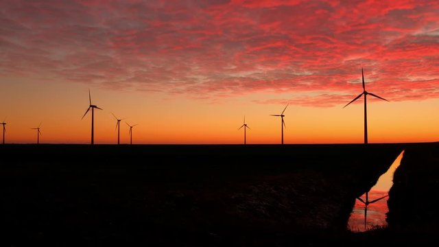 Wind Turbines Generating Green Energy at Sunset with Reflection in a Canal and Beautiful Red Clouds in the Sky in Almere Pumpus, Netherlands