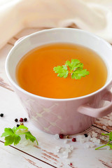 Cooked hot bone broth with spices and fresh herbs. Medical dietary broth and superfood. For ketogenic diet and paleo diet. Serve on an individual plate on a wooden background and with a white napkin.