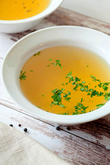 Cooked hot bone broth with spices and fresh herbs. Medical dietary broth and superfood. For ketogenic diet and paleo diet. Serve on an individual plate on a wooden background and with a white napkin.