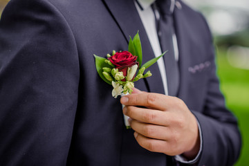 At the wedding, the bride straightens the flower in the outer pocket of the groom's jacket. Close-up.