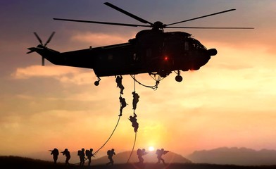 Military commando helicopter drops in silhouette during sunset