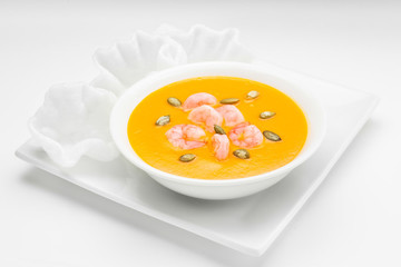  Pumpkin cream soup with shrimp and pumpkin seeds in a white bowl on a white background