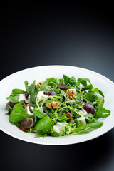  Salad with vegetables and arugula and feta cheese with walnuts in a white plate on a dark background