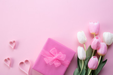 Happy mothers day concept. Top view of pink tulip flowers, gift box and paper heart on pink pastel background. Flat lay.