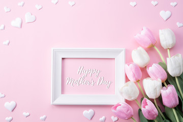 Happy mothers day concept. Top view of pink tulip flowers and white picture frame with happy mothers day text on pink pastel background. Flat lay.