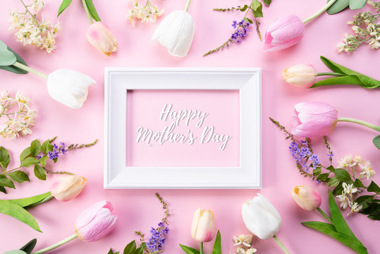 Happy mothers day concept. Top view of pink tulip flowers and white picture frame with happy mothers day text on pink pastel background. Flat lay.