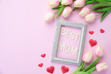 Happy mothers day concept. pink tulip flower with paper heart and Picture Frame with BEST MOM text on pink pastel background.