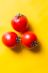 Ripe red tomatoes with green leaves isolated on yellow background. Top view.