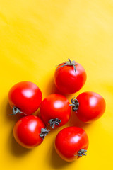 Ripe red tomatoes with green leaves isolated on yellow background. Top view.