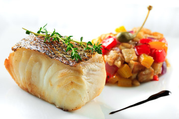 Fried fish slice with vegetable garnish on a white plate