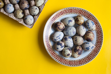Quail eggs container and fresh eggs on yellow background. Top view.