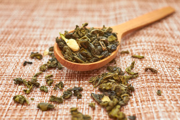 The composition of natural tea with jasmine. A macro photo of tea petals on a wooden spoon with...