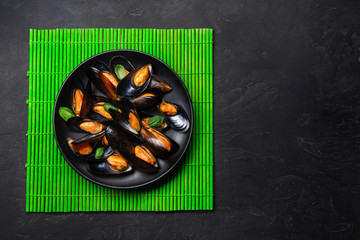 Seafood mussels and basil leaves in a black plate on bamboo mat and stone table