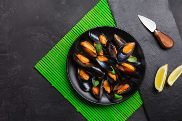 Seafood mussels, basil leaves in a black plate with lemon and knife on green bamboo mat and stone table