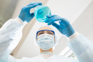 Directly below view of serious concentrated lady chemist in protective mask and goggles holding...