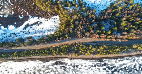 Fototapeta na wymiar Aerial view of spring rural road in yellow pine forest with melting ice lake