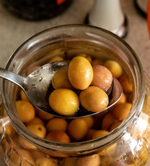 green scratched olives and spoon in jar, close-up,