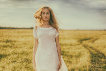 Fototapeta na wymiar Portrait of beautiful girl in field. Beautiful blond girl on green field with flowers. Rural scene