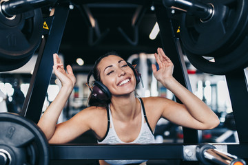 Fototapeta na wymiar Young fit and attractive woman working out in modern gym and listening to music with bluetooth headphones and smart phone.