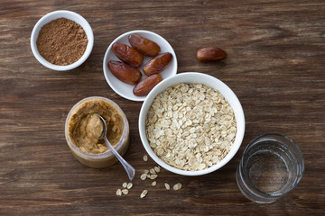 Raw oatmeal in a white bowl, peanut butter, dates fruits, cocoa and a glass of water, ingredients for delicious chocolate porridge