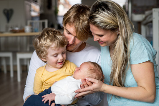 Young parents with newborn baby and small toddler son at home.
