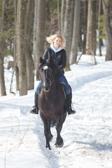 Fototapeta na wymiar A winter forest. A young blonde woman riding a horse on snowy ground