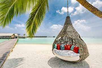 Chill lounge zone on the sandy beach, Maldives island. Beautiful tropical Maldives beach under cloudy sky with swings on coconut palm. Luxury vacation