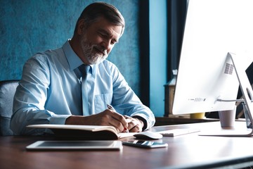 Mature businessman looking and analyzing document in his modern office at work.