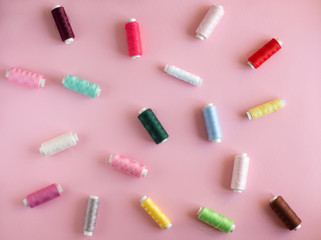 Many bobbins of bright sewing thread with a soft pink background
