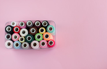 Many bobbins of bright sewing thread with a soft pink background