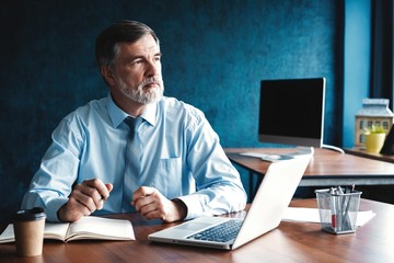 Focused mature businessman deep in thought while sitting at a table in modern office.