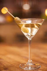 Closeup of a martini glass with olives on a wooden table in a resturant