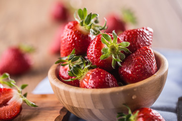Juicy washed strawberries in wooden bowl on kitchen table