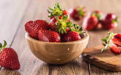 Juicy washed strawberries in wooden bowl on kitchen table
