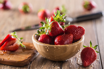 Juicy washed strawberries in wooden bowl on kitchen table