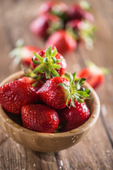 Juicy washed strawberries in wooden bowl on kitchen table