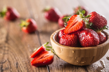 Juicy washed strawberries in wooden bowl on kitchen table