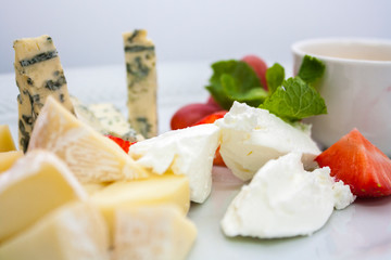 a plate of several kinds of cheeses in assortment, with strawberries and grapes, on a white plate on a white background, close-up