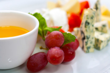 grapes and a cup with melted butter on the background of a plate with several types of cheese in an assortment, close-up