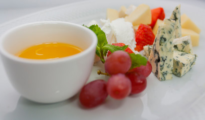 a plate of several kinds of cheeses in assortment, with strawberries and grapes, on a white plate on a white background, close-up