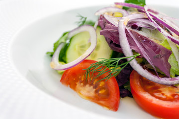 vegetable salad of tomato, cucumber and onion rings, with dill and parsley, seasoned with butter, on a white plate, on a white background, side view, close-up