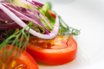 close-up of a slice of tomato in a vegetable salad made of tomato, ogutz and onion rings, with dill and parsley, seasoned with butter, on a white plate, on a white background, side view
