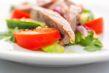 a drop of clear olive oil hangs on the tip of a piece of ham in a vegetable salad of meat and vegetables