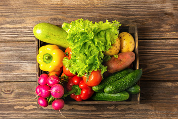 Fresh vegetables greens in a box on a wooden background. Autumn harvest. Flat layout. View from...