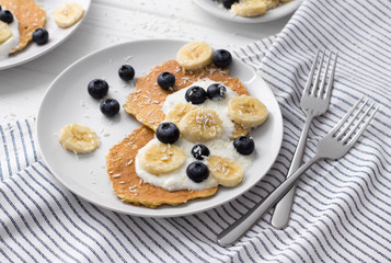 Homemade oatmeal pancakes with yogurt, fresh blueberry and banana at white wooden background.