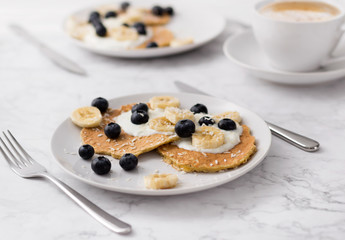 Two plates of homemade breakfast with forest fruits  and cup of coffee at marble table.