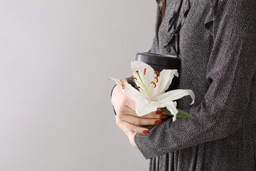 Woman with mortuary urn and lily flower on light background - obrazy, fototapety, plakaty