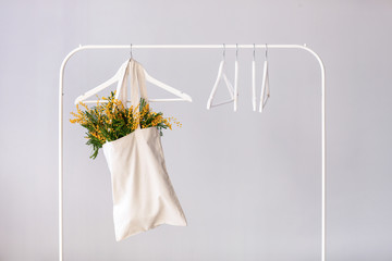 Bag with bouquet of mimosa flowers hanging on rack against light background