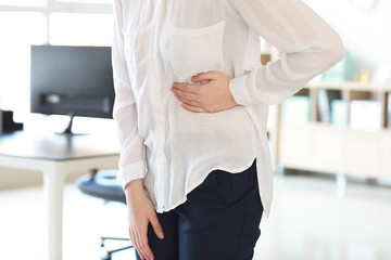 Young woman suffering from stomachache in office - obrazy, fototapety, plakaty
